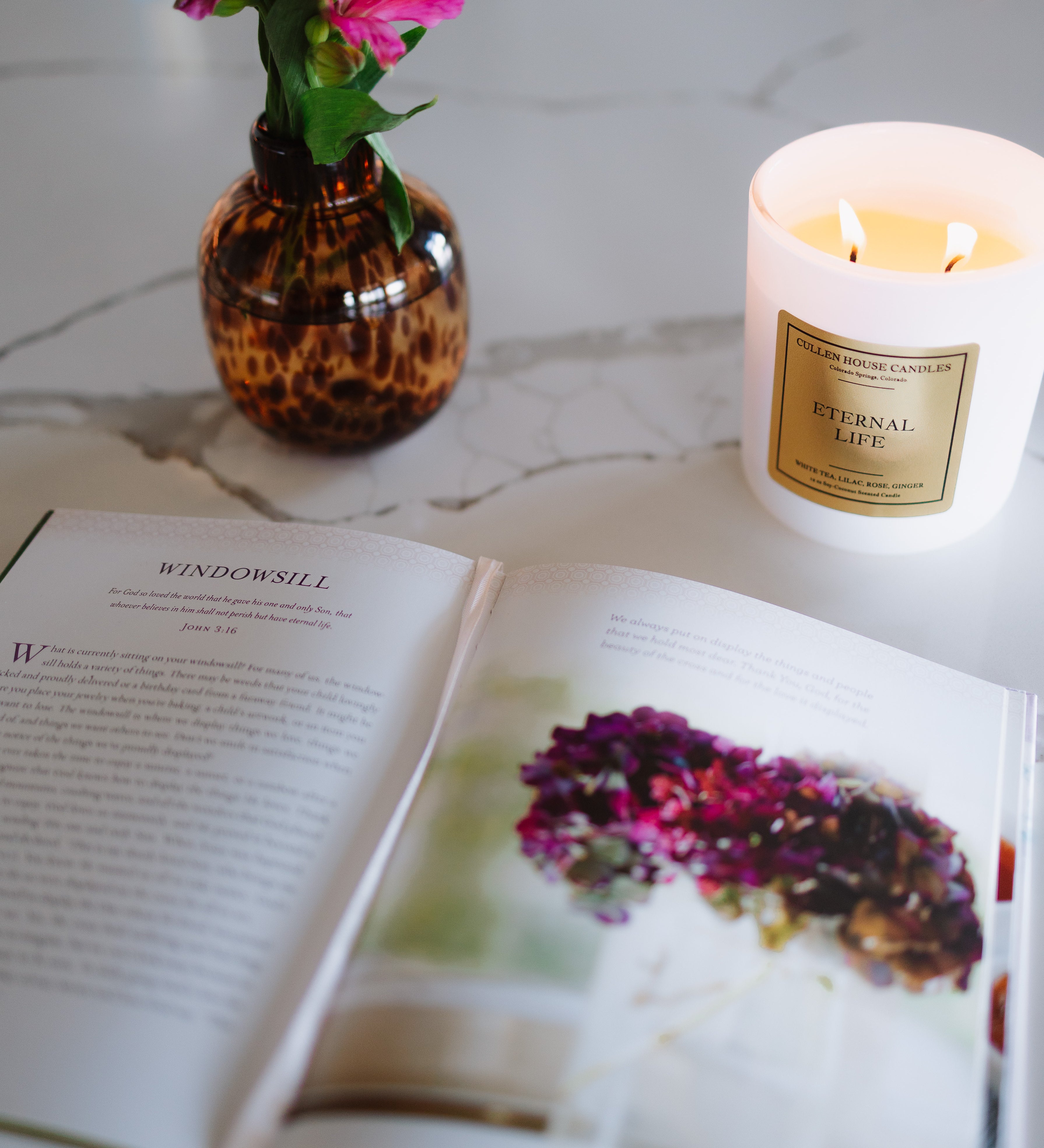 Open book with a candle and vase of flowers on a marble surface