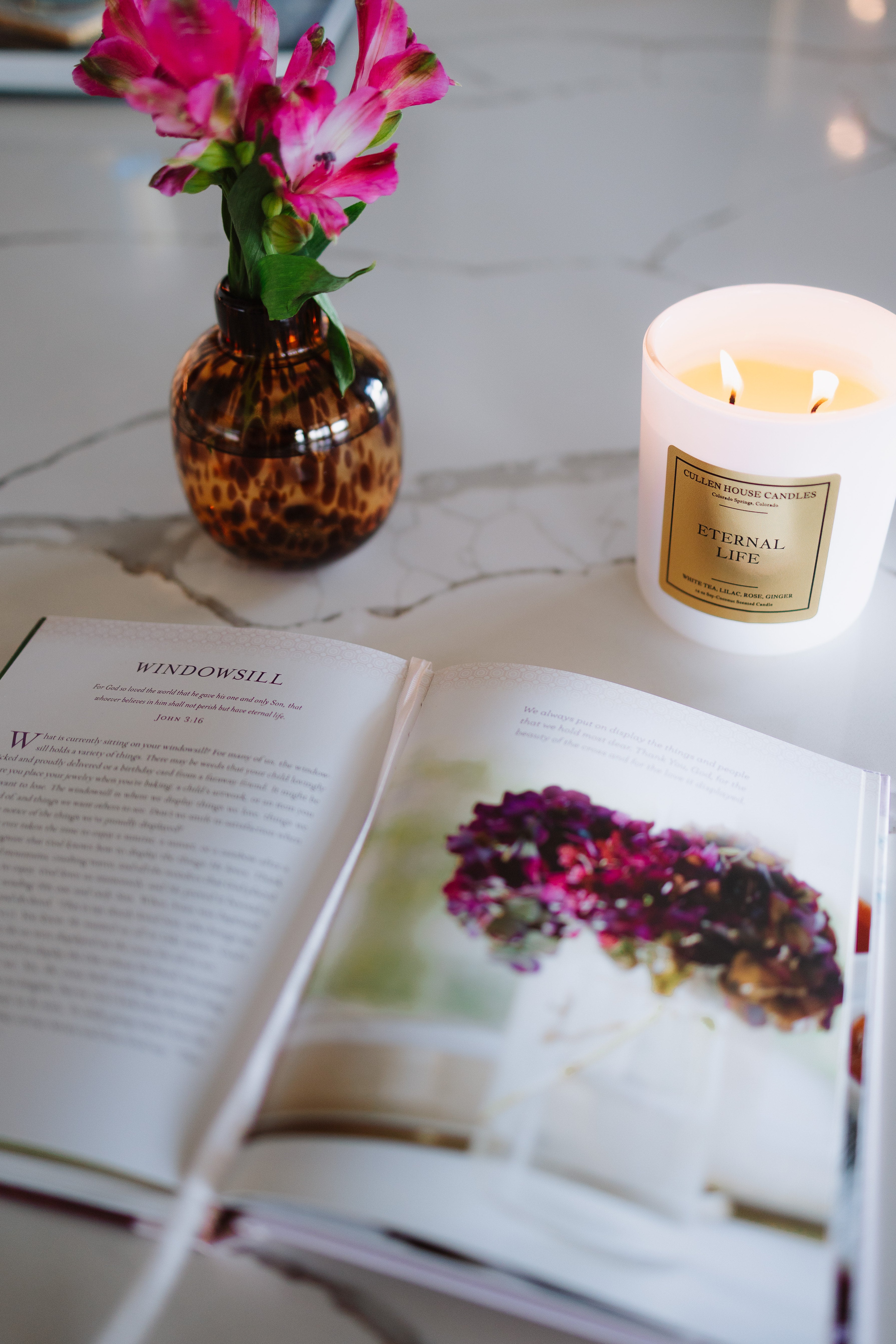 Open book with a candle and vase of flowers on a marble surface