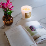 Candle, vase with flowers, and open book on a marble surface