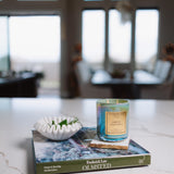 Candle on a book with decorative bowl on a marble surface, blurred room background