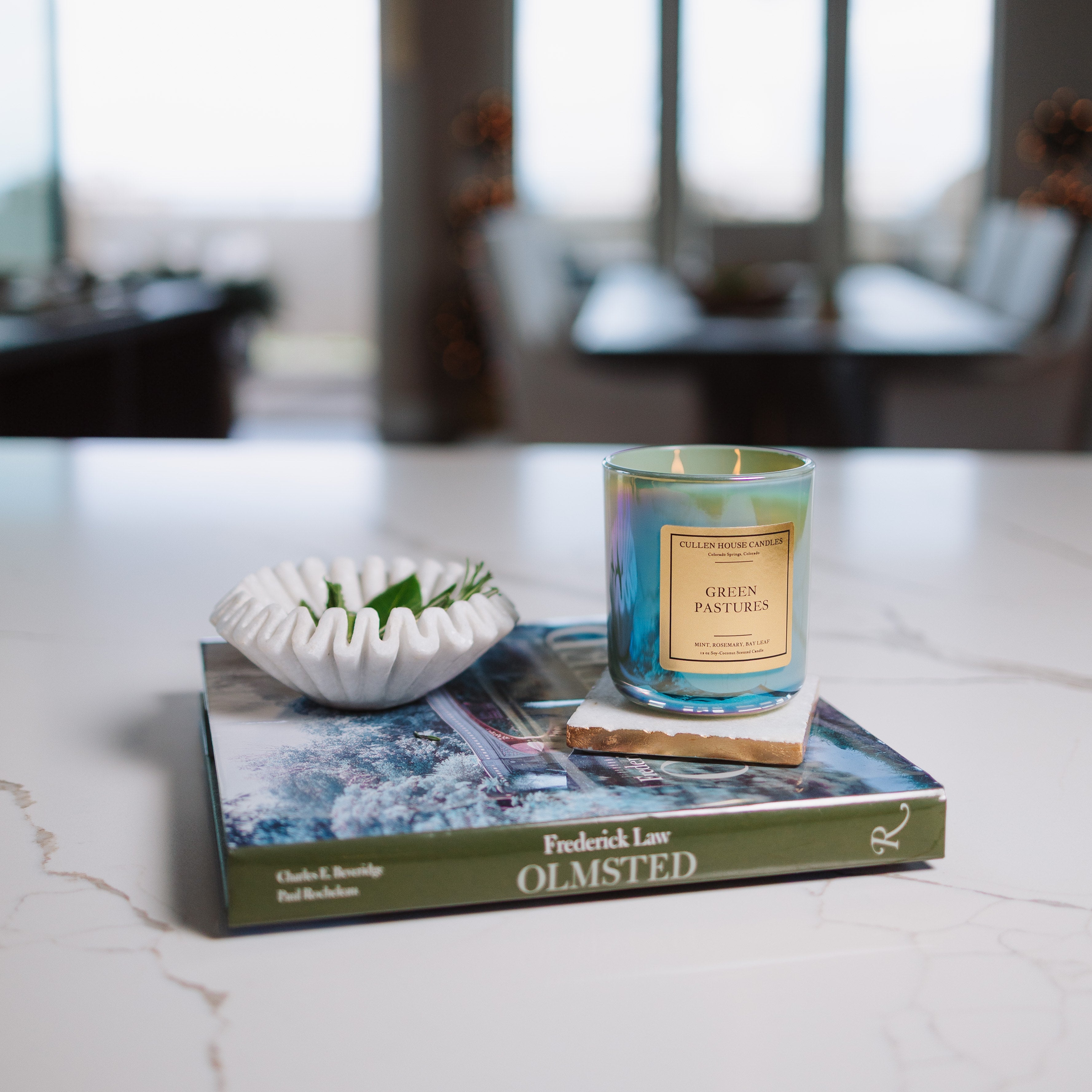 Candle on a book with decorative bowl on a marble surface, blurred room background