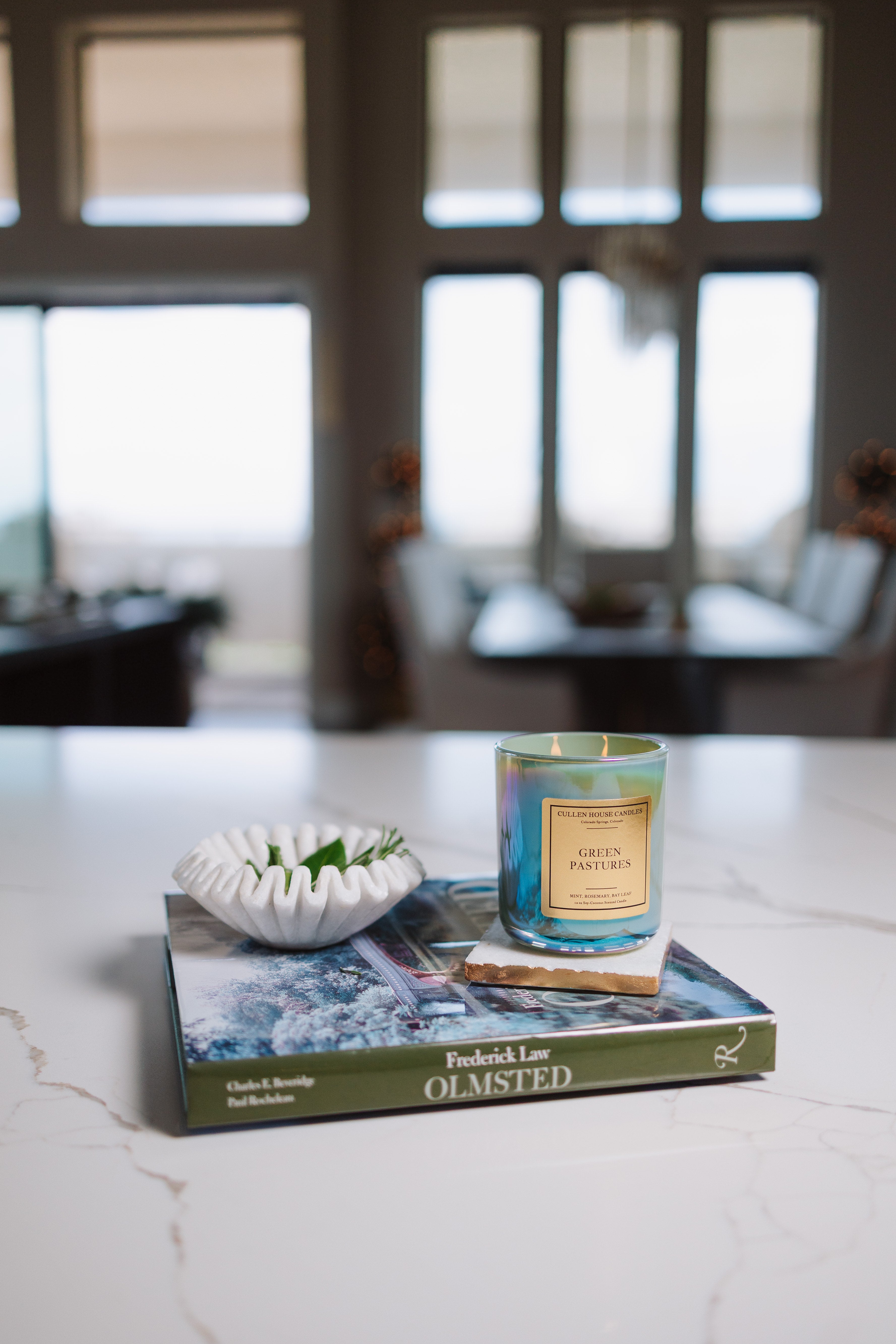 Candle on a book with decorative bowl on a marble surface, blurred room background