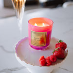 Candle labeled 'Banquet of Love' on a white dish with raspberries and strawberries, next to a cocktail.