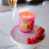 Candle labeled 'Banquet of Love' on a white dish with raspberries and strawberries, next to a cocktail.