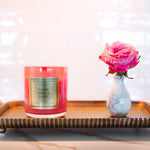 Pink candle and vase with pink flower on a decorative tray against a blurred background