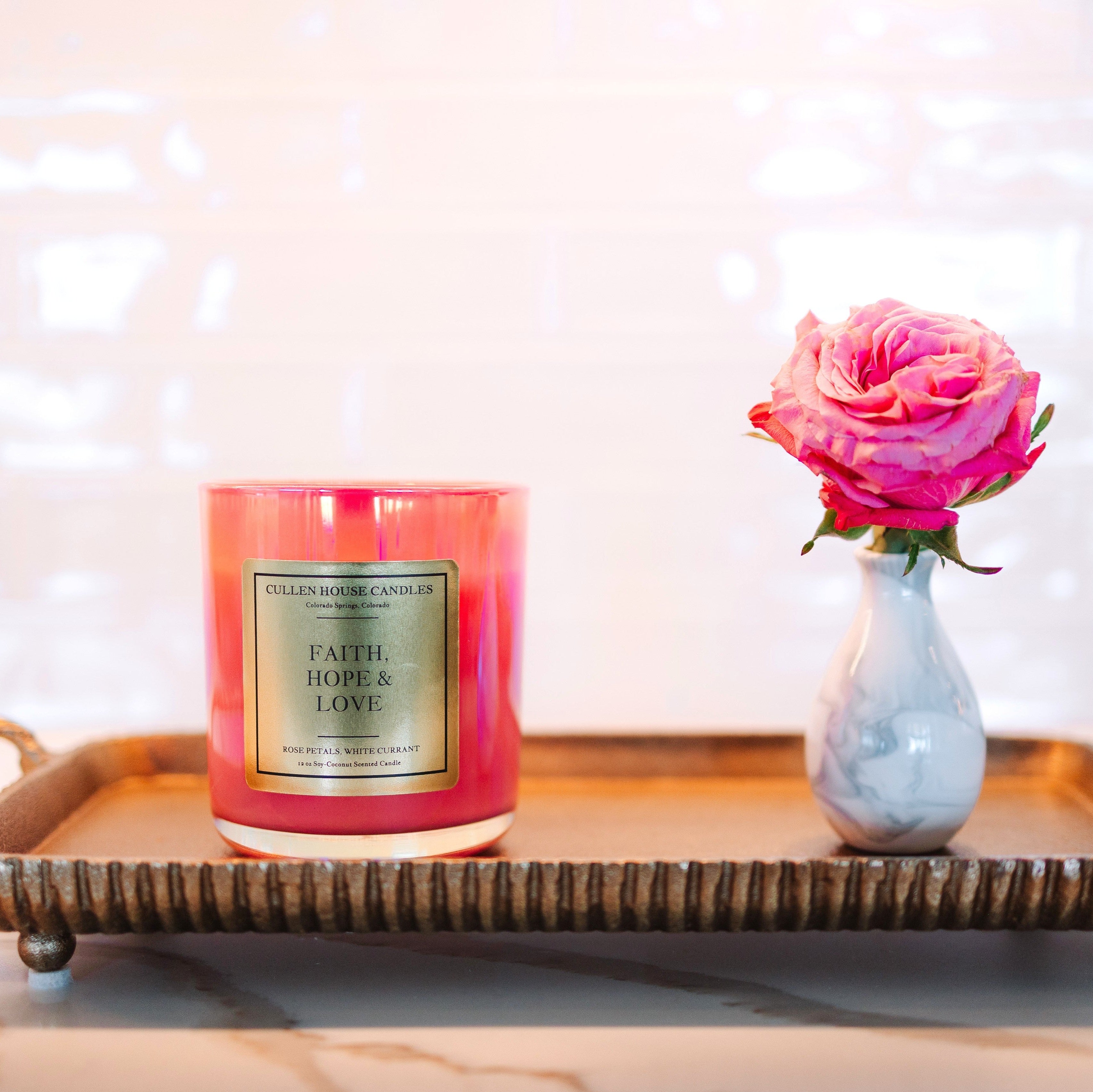 Pink candle and vase with pink flower on a decorative tray against a blurred background