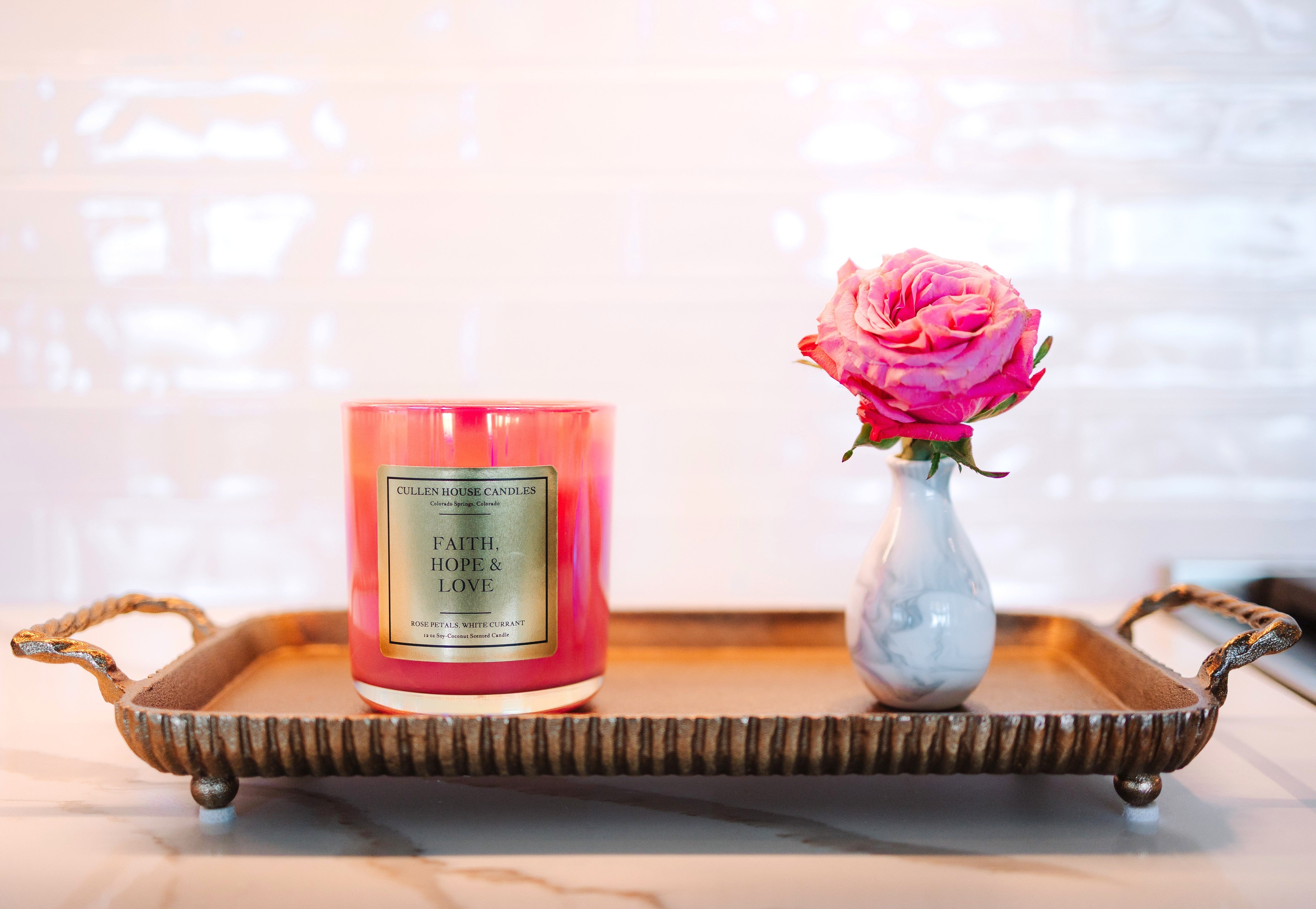 Pink candle and vase with pink flower on a decorative tray against a blurred background