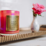 Candle with 'Faith, Hope & Love' label on a decorative tray with a blurred background