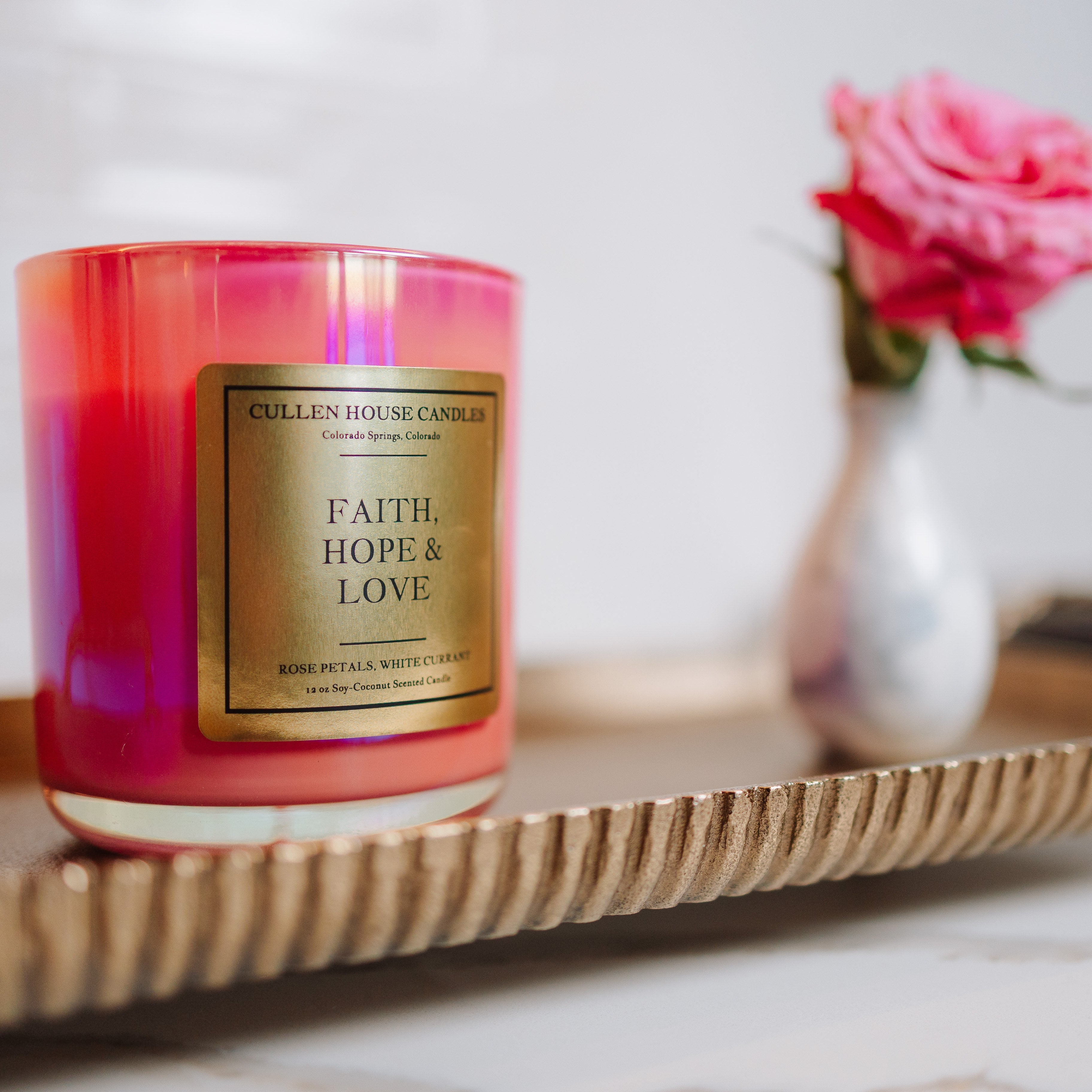 Candle with 'Faith, Hope & Love' label on a decorative tray with a blurred background