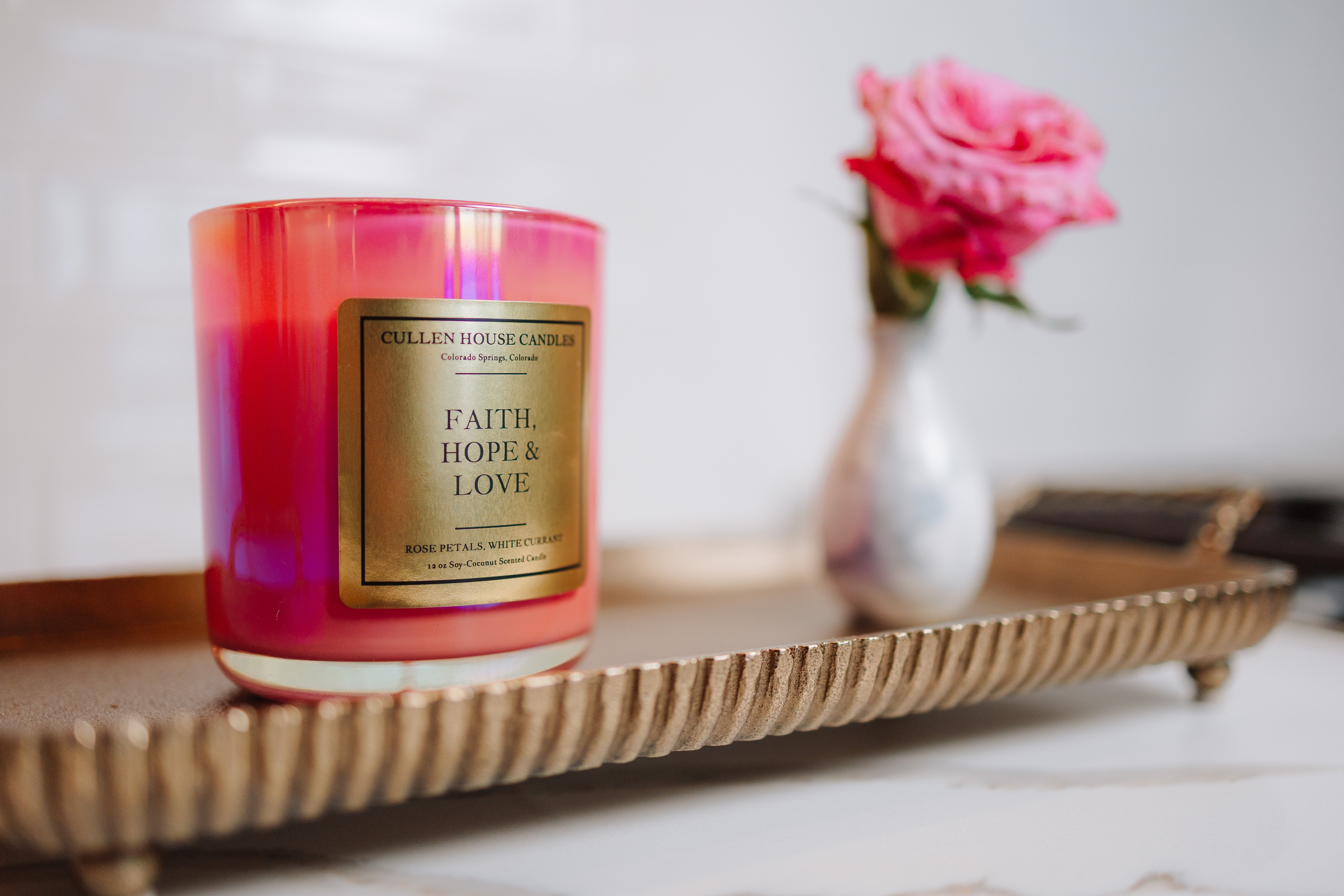 Candle with 'Faith, Hope & Love' label on a decorative tray with a blurred background