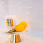 Candle labeled 'Eightless Paths' on a marble stand with lemons against a tiled wall.