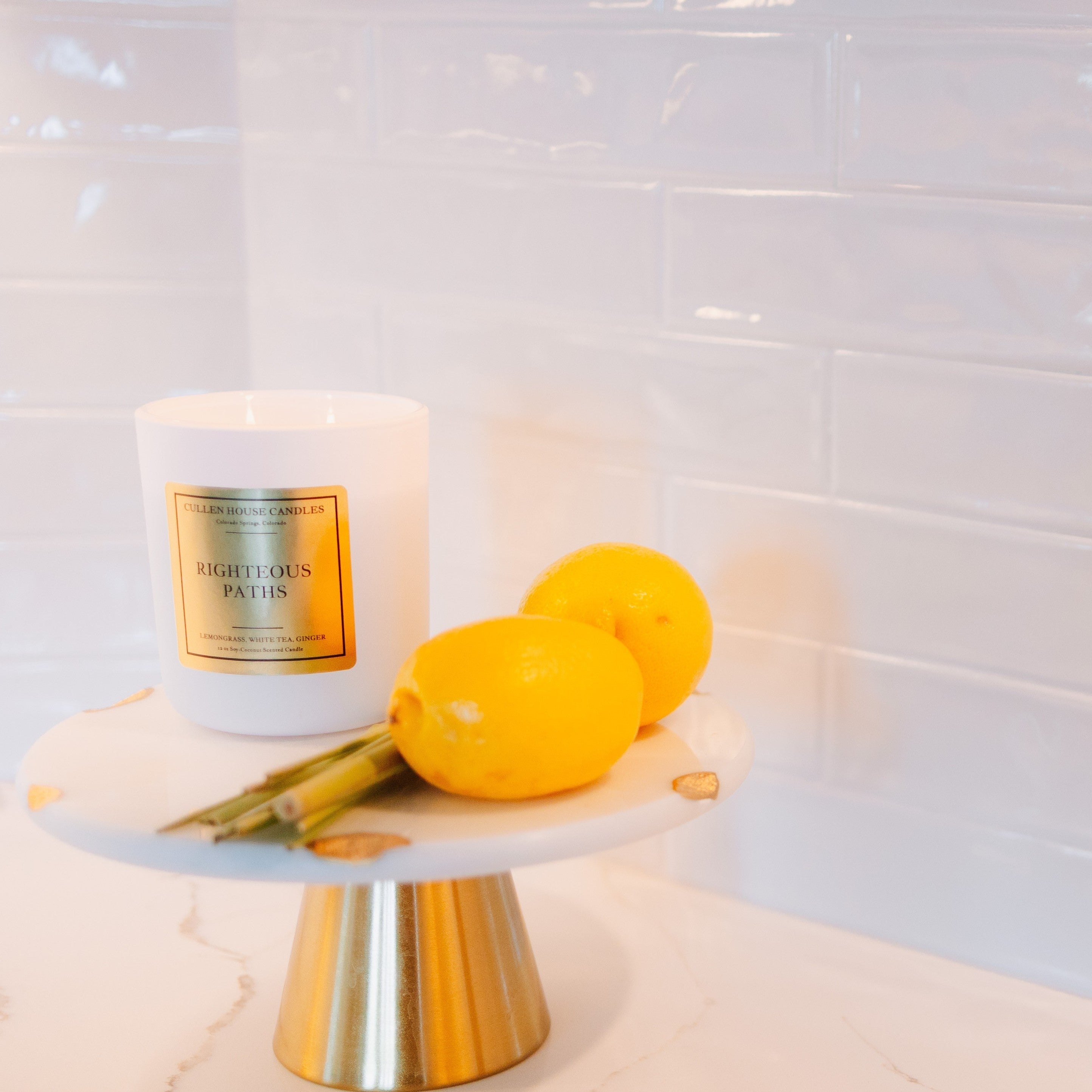 Candle labeled 'Eightless Paths' on a marble stand with lemons against a tiled wall.