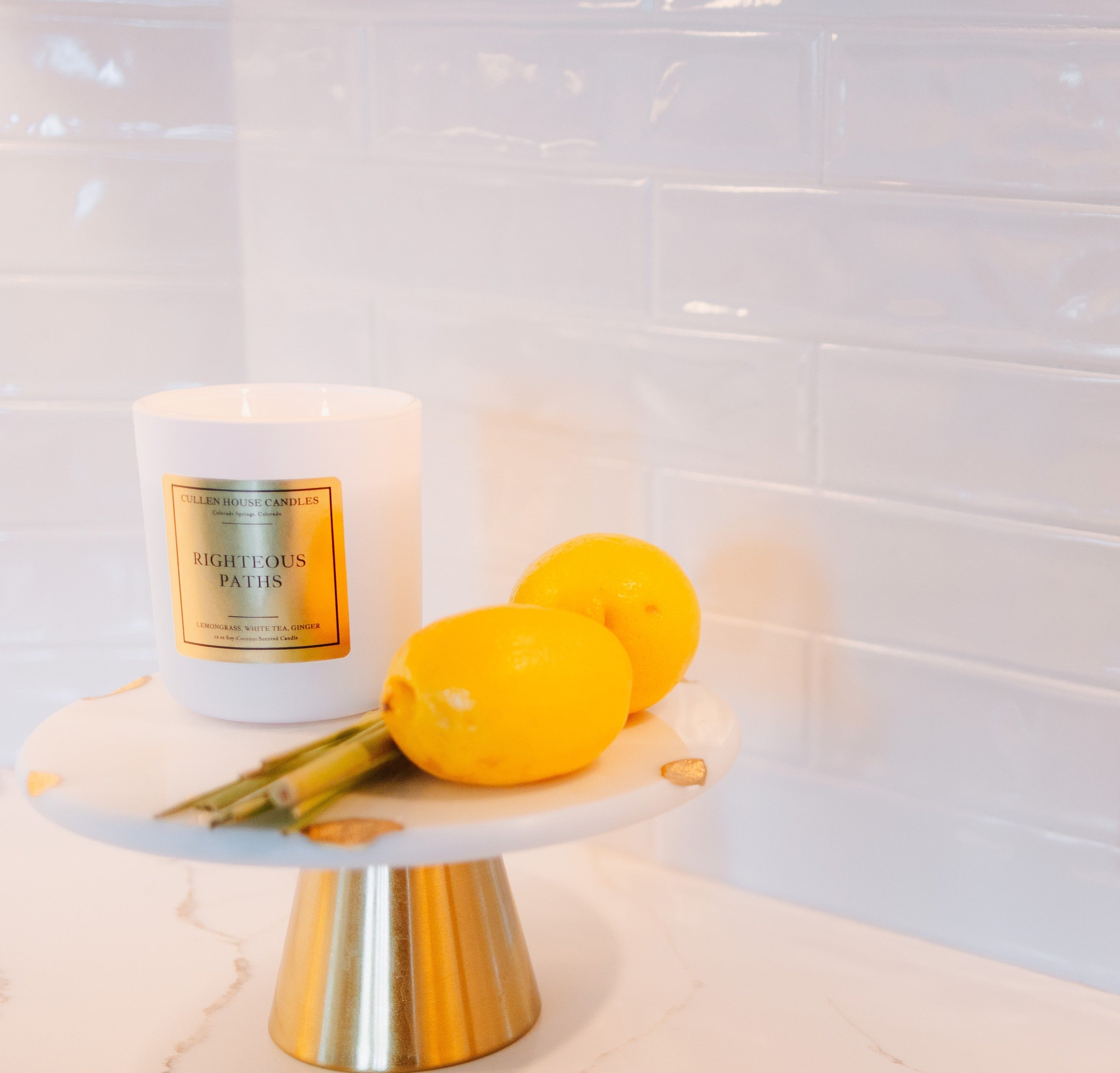 Candle labeled 'Eightless Paths' on a marble stand with lemons against a tiled wall.