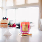 Candle labeled 'Taste the Rainbow' on a table with a cake and fruit in the background