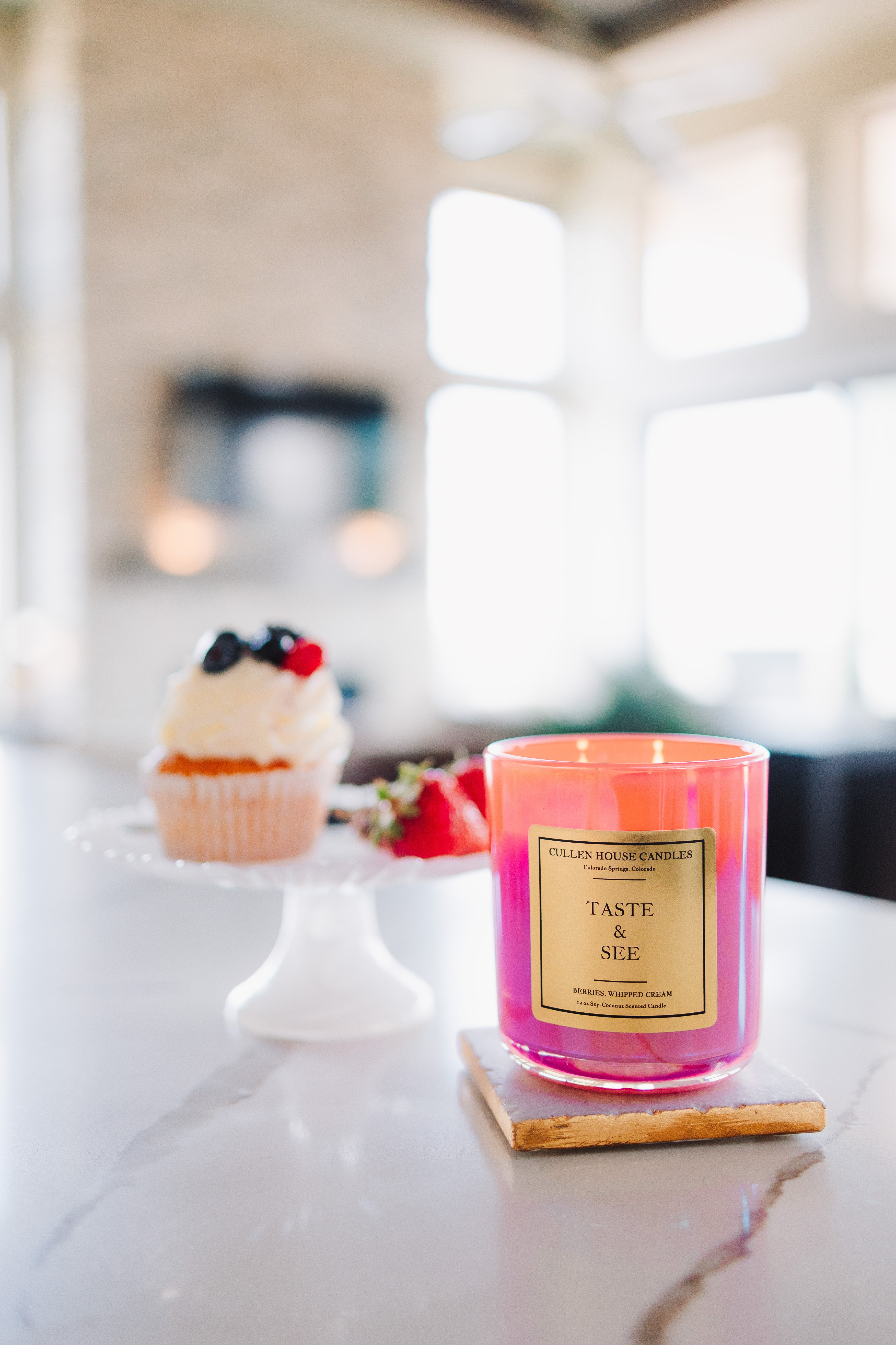 Pink candle labeled 'Taste & See' on a kitchen counter with a blurred background