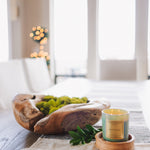 Decorative setting with a wooden bowl, candle, and greenery on a table.