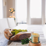 Decorative setting with a wooden bowl, candle, and greenery on a table.