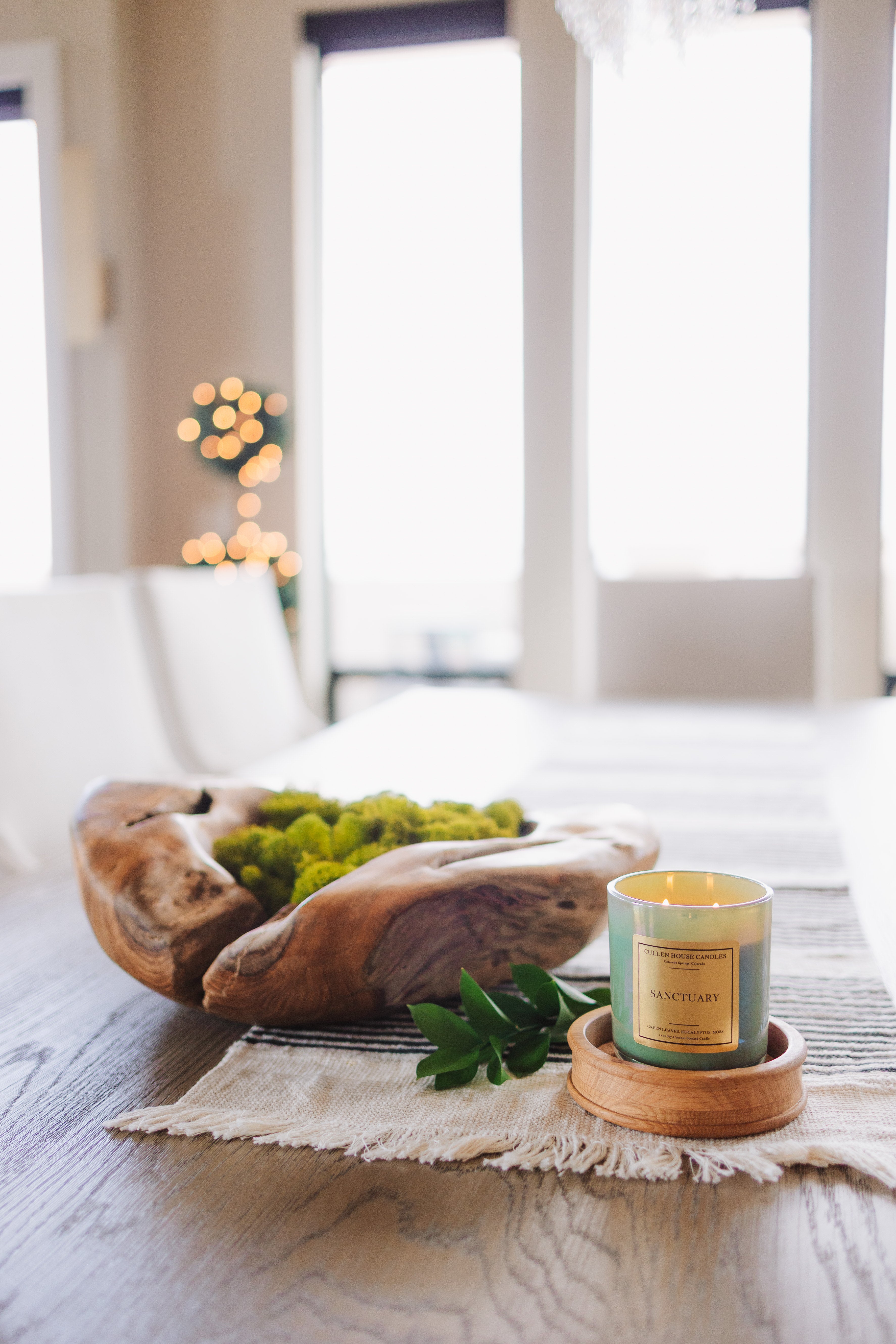 Decorative setting with a wooden bowl, candle, and greenery on a table.