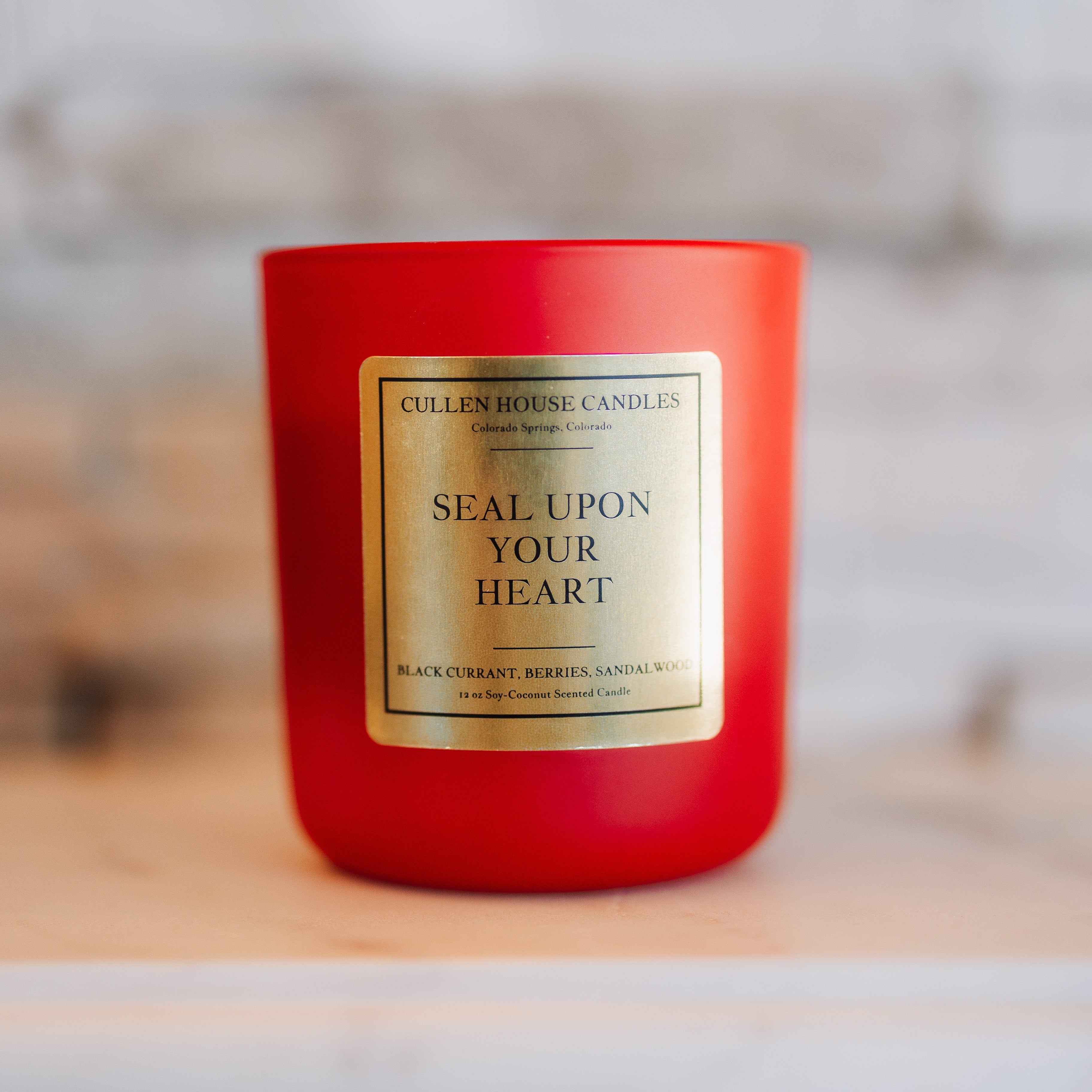 Red candle with a gold label on a wooden surface