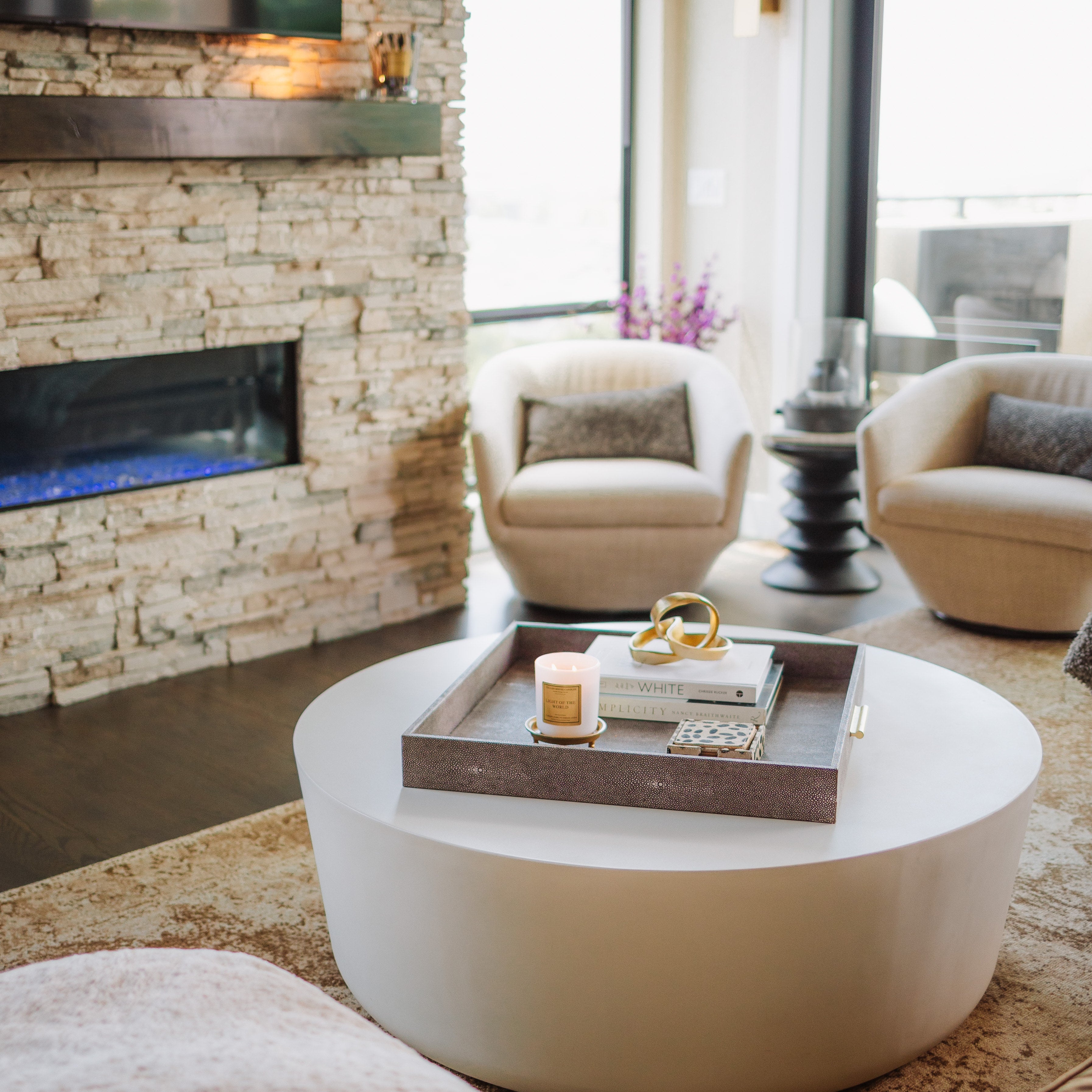 Modern living room with a stone fireplace, white coffee table, and armchairs.