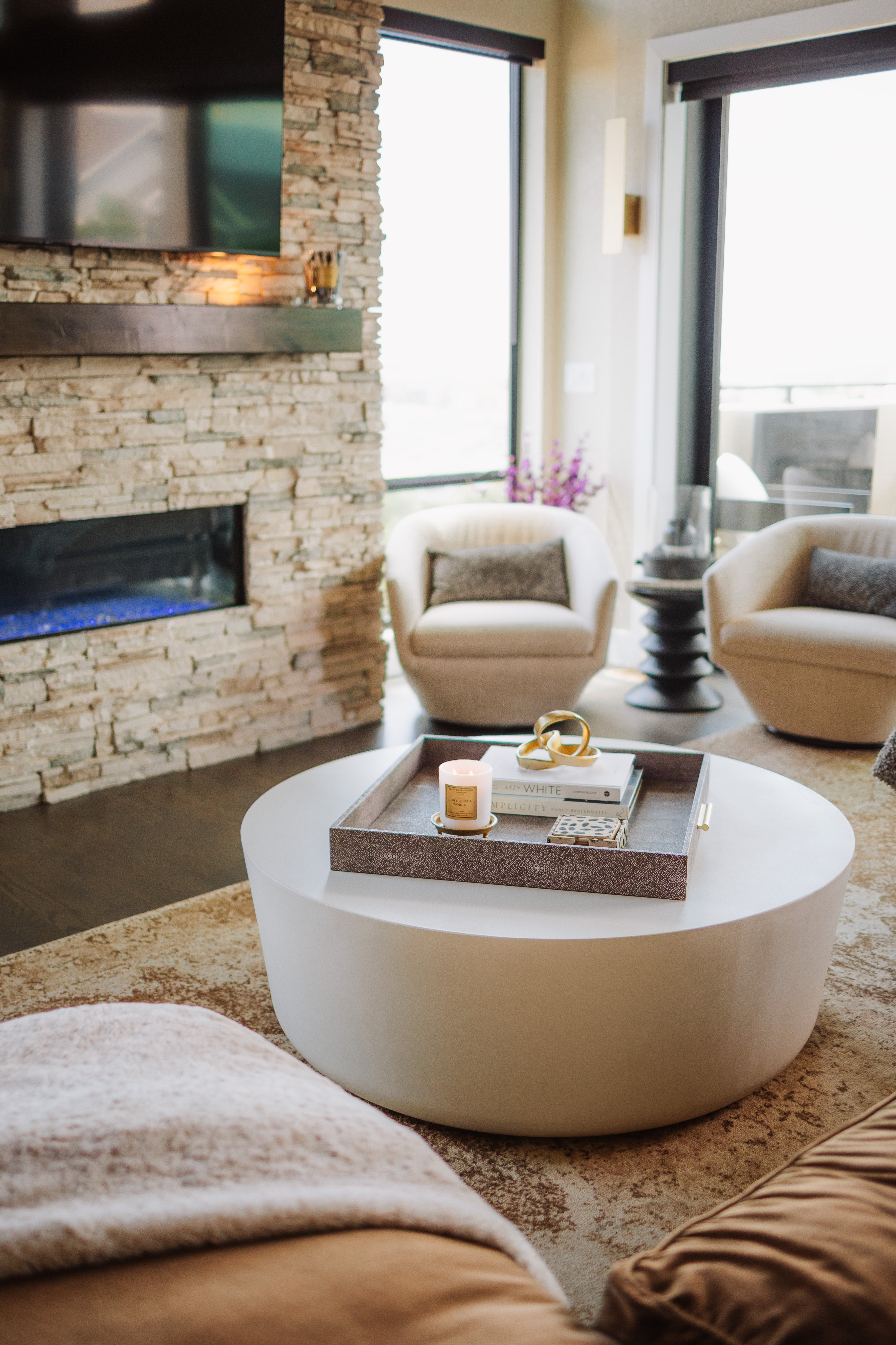Modern living room with a stone fireplace, white coffee table, and armchairs.