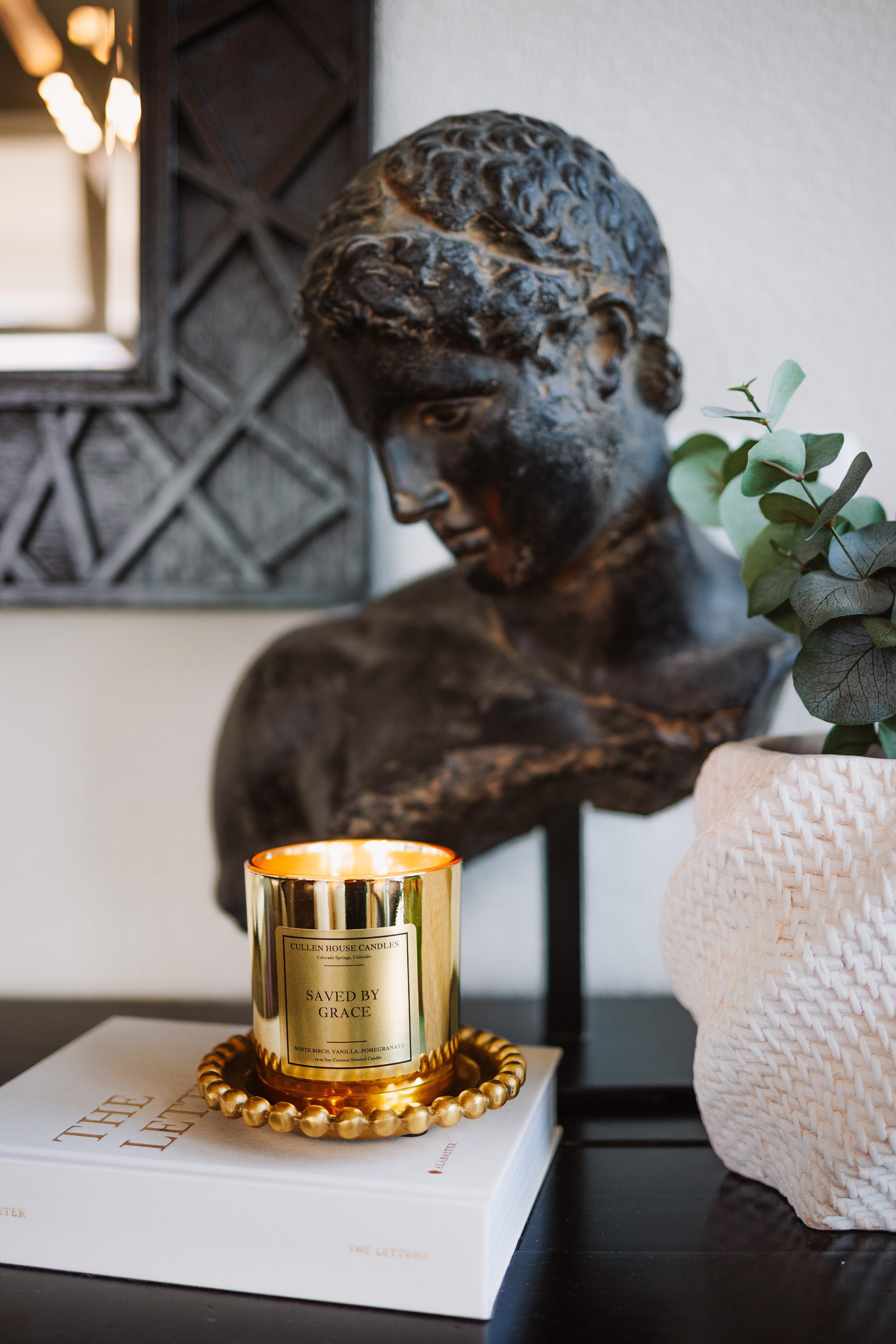 Candle with decorative label on a book next to a classical statue and plant