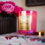 Pink candle labeled 'Mary Magdalene' on a floral-patterned book with pink flowers in the background.