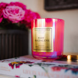Pink candle labeled 'Mary Magdalene' on a floral-patterned book with pink flowers in the background.