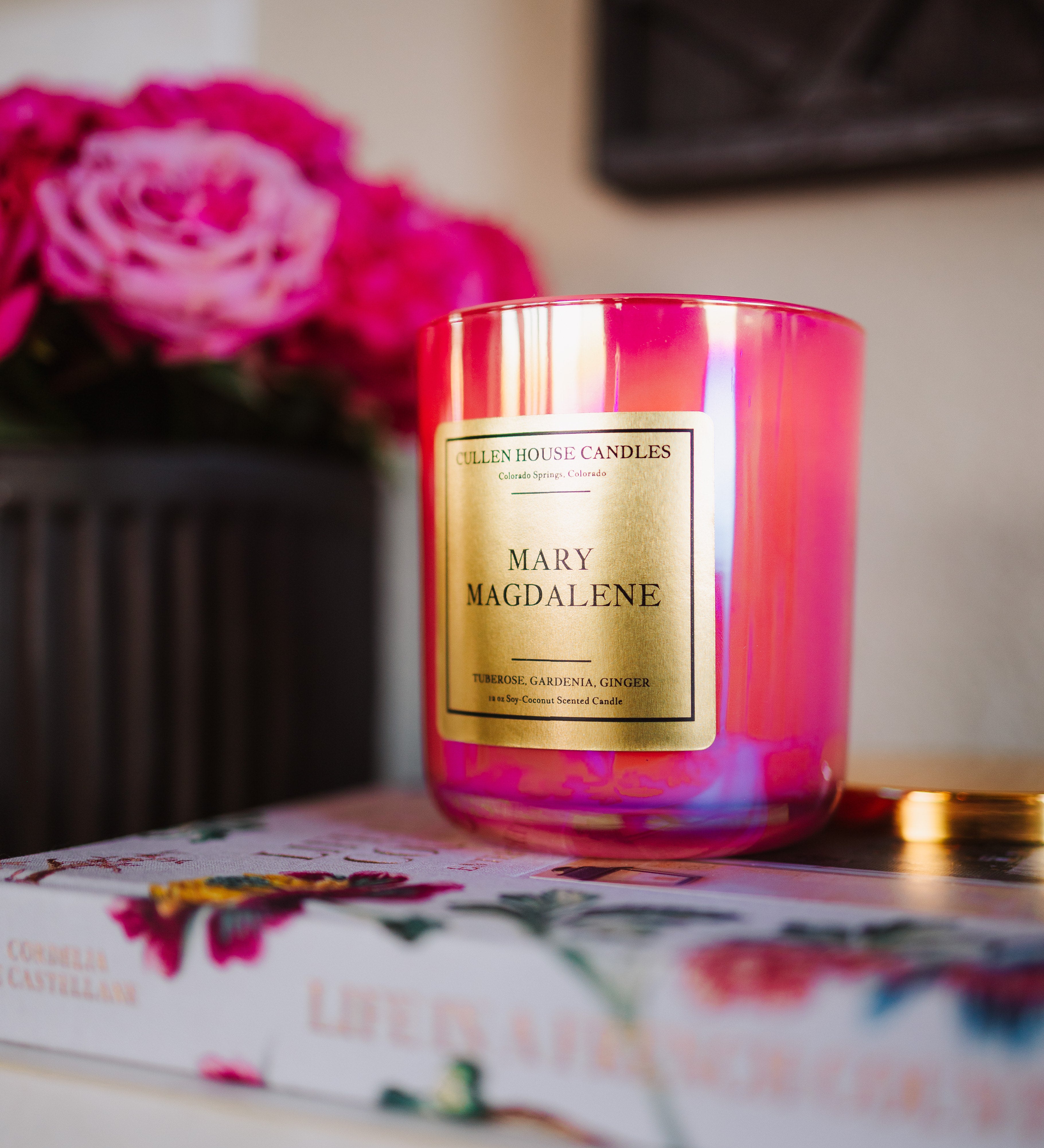 Pink candle labeled 'Mary Magdalene' on a floral-patterned book with pink flowers in the background.