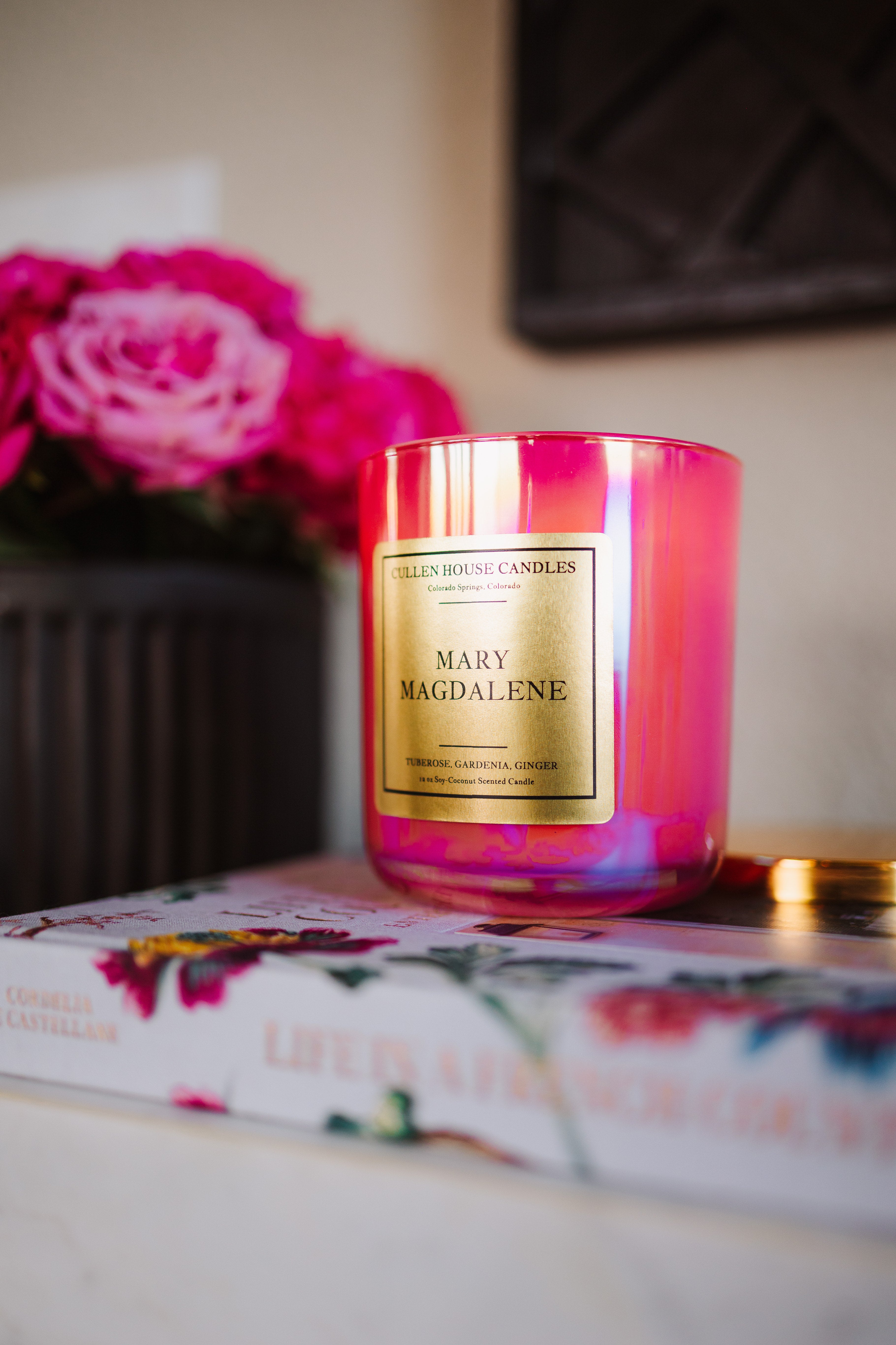 Pink candle labeled 'Mary Magdalene' on a floral-patterned book with pink flowers in the background.