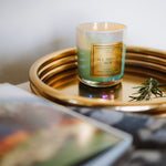 Candle labeled 'All Things New' on a gold tray with a blurred background