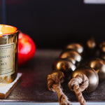 Gold candle with a label on a wooden coaster next to decorative items.
