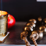Gold candle with a label on a wooden coaster next to decorative items.