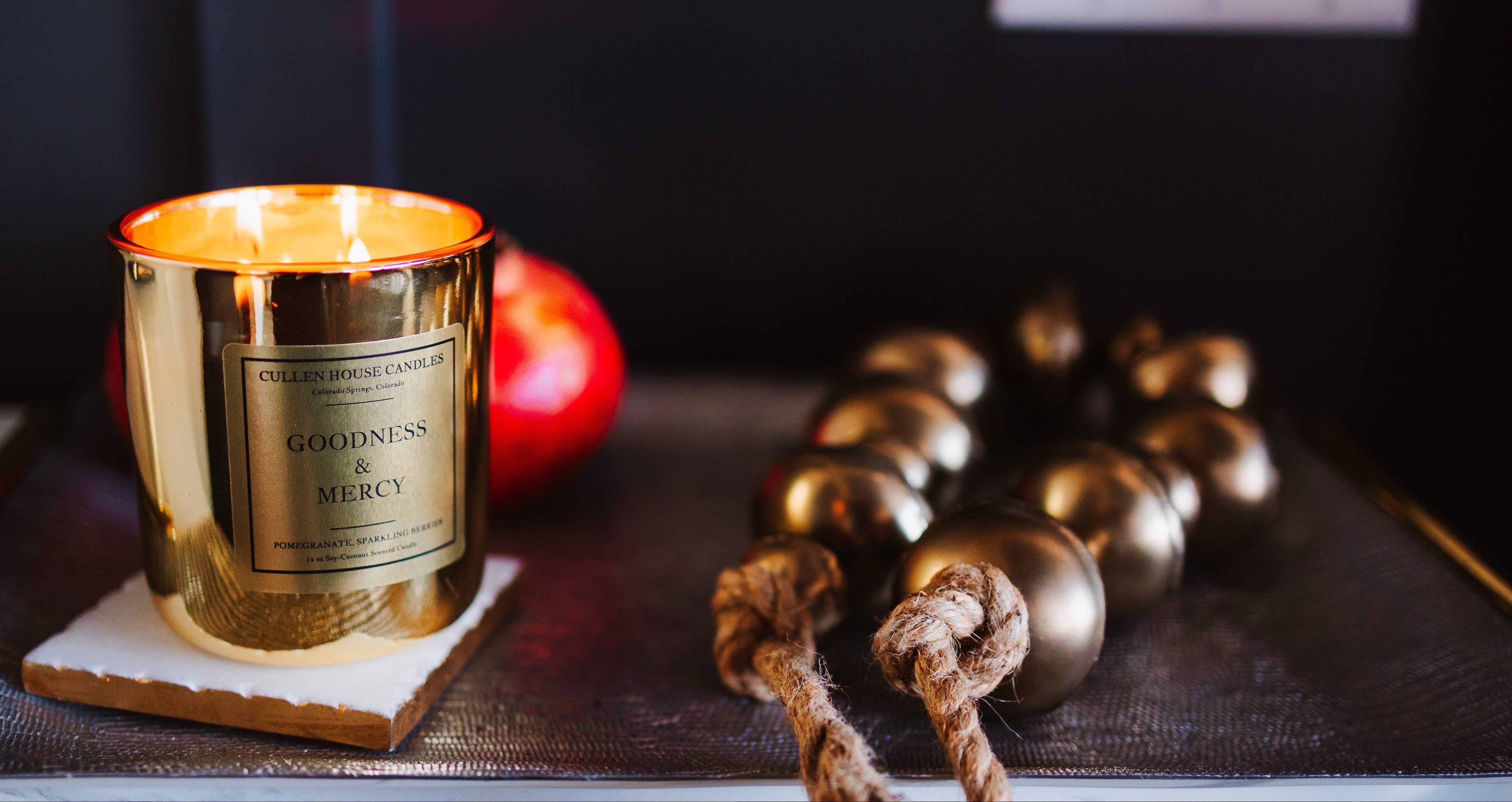 Gold candle with a label on a wooden coaster next to decorative items.