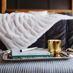 Tray with a book and candle on a bed with striped bedding