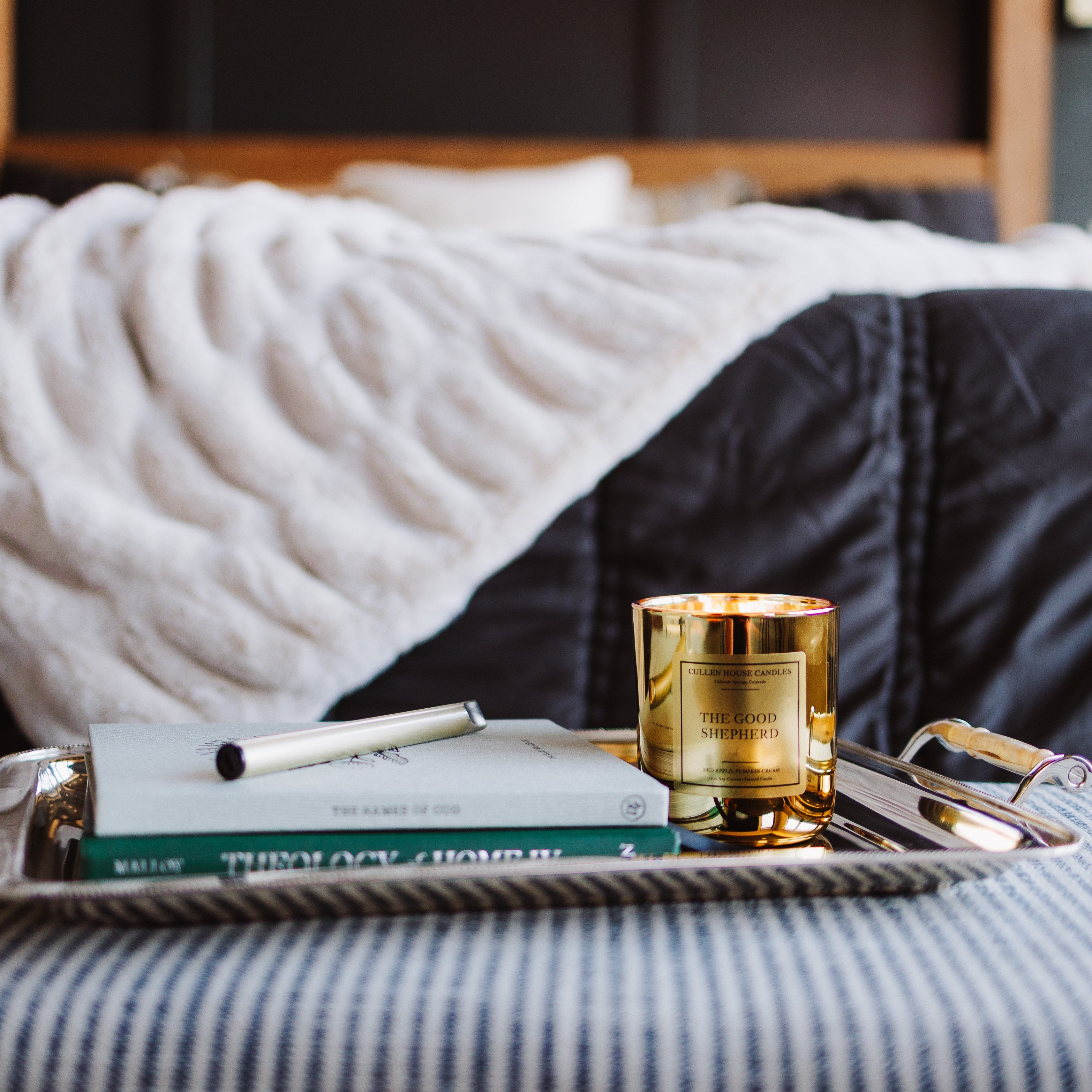 Tray with a book and candle on a bed with striped bedding