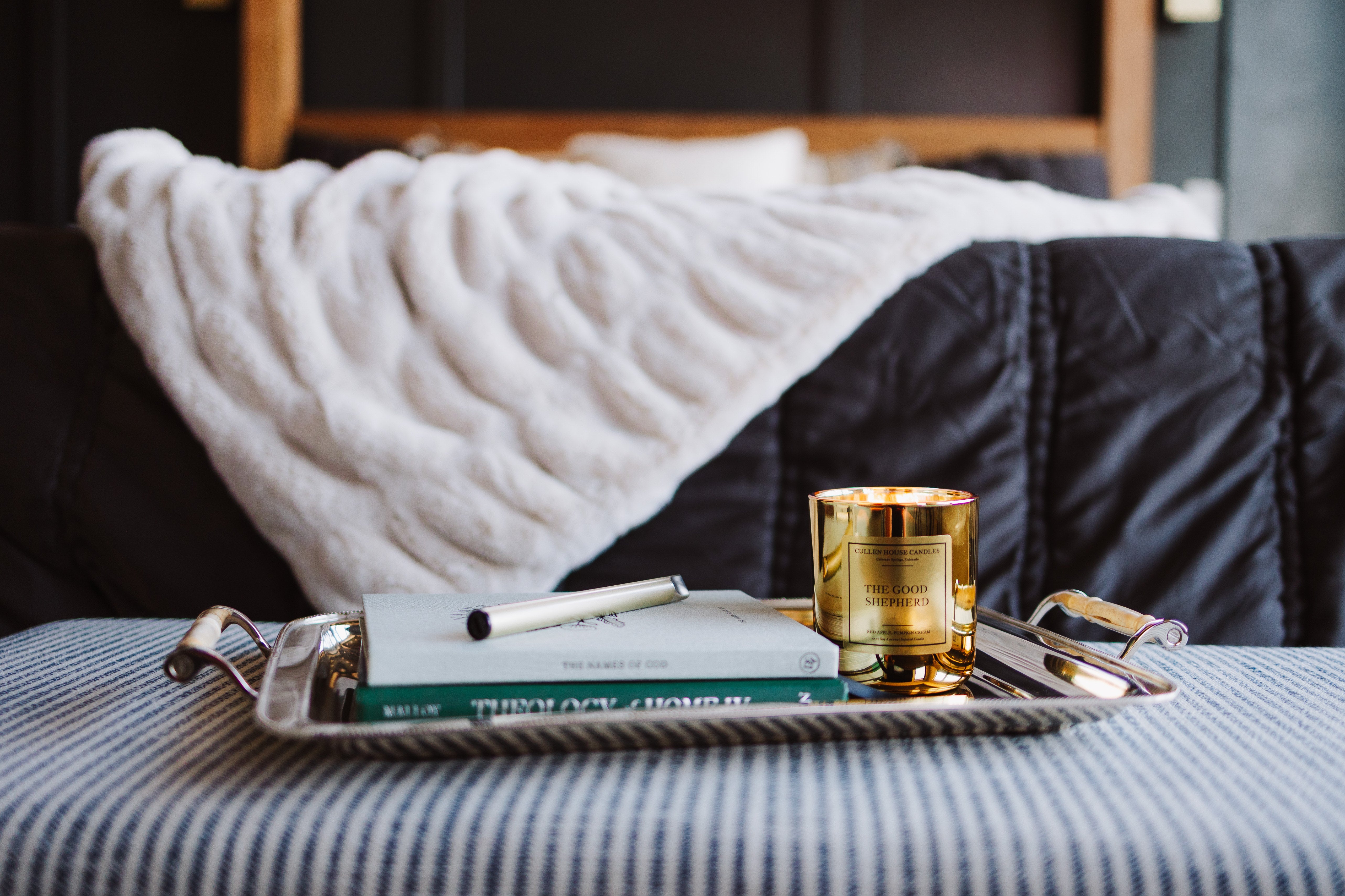 Tray with a book and candle on a bed with striped bedding