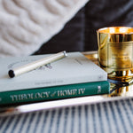 Gold candle on a tray with books and a pen