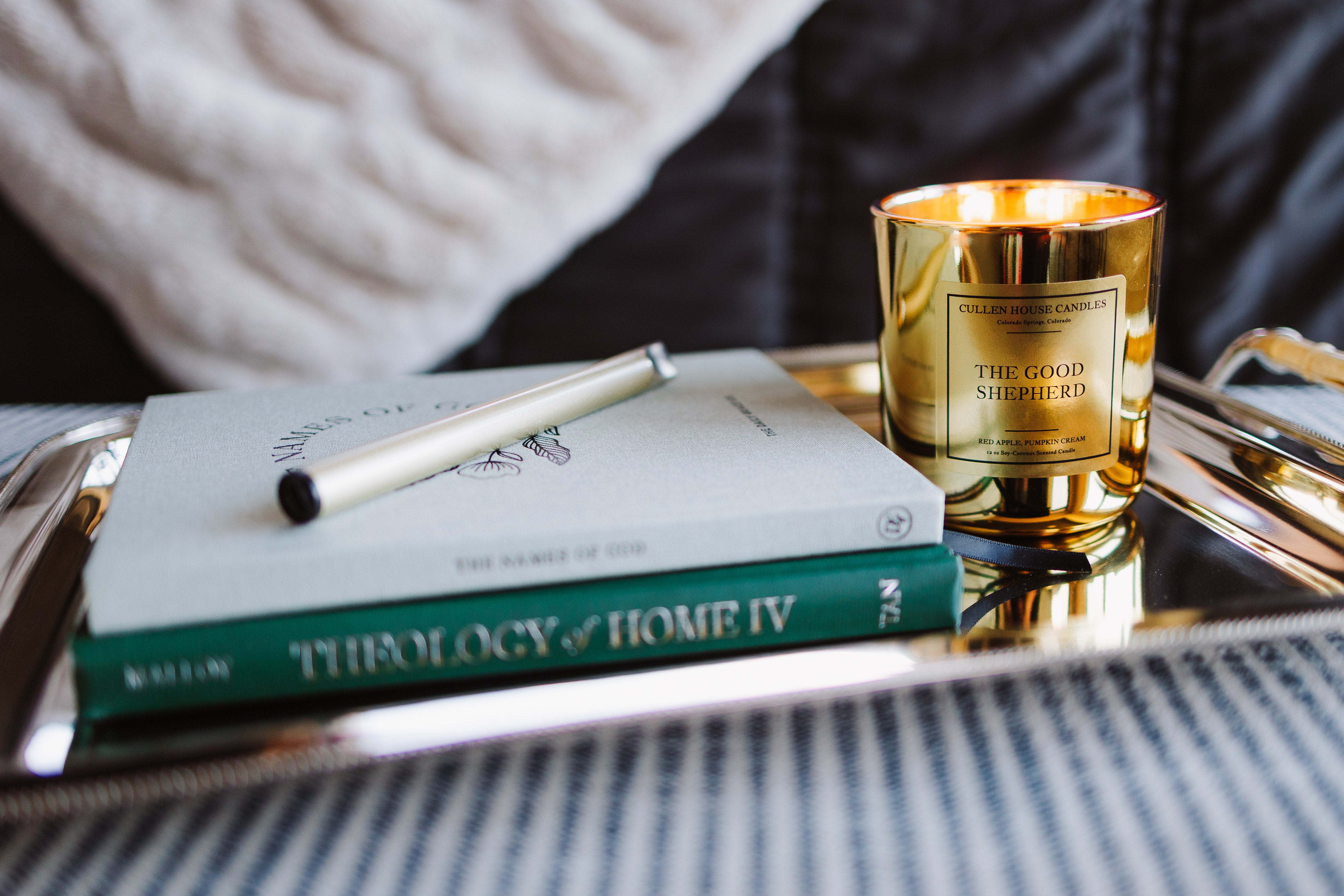Gold candle on a tray with books and a pen
