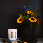 Candle with a decorative label and a vase of flowers on a dark background