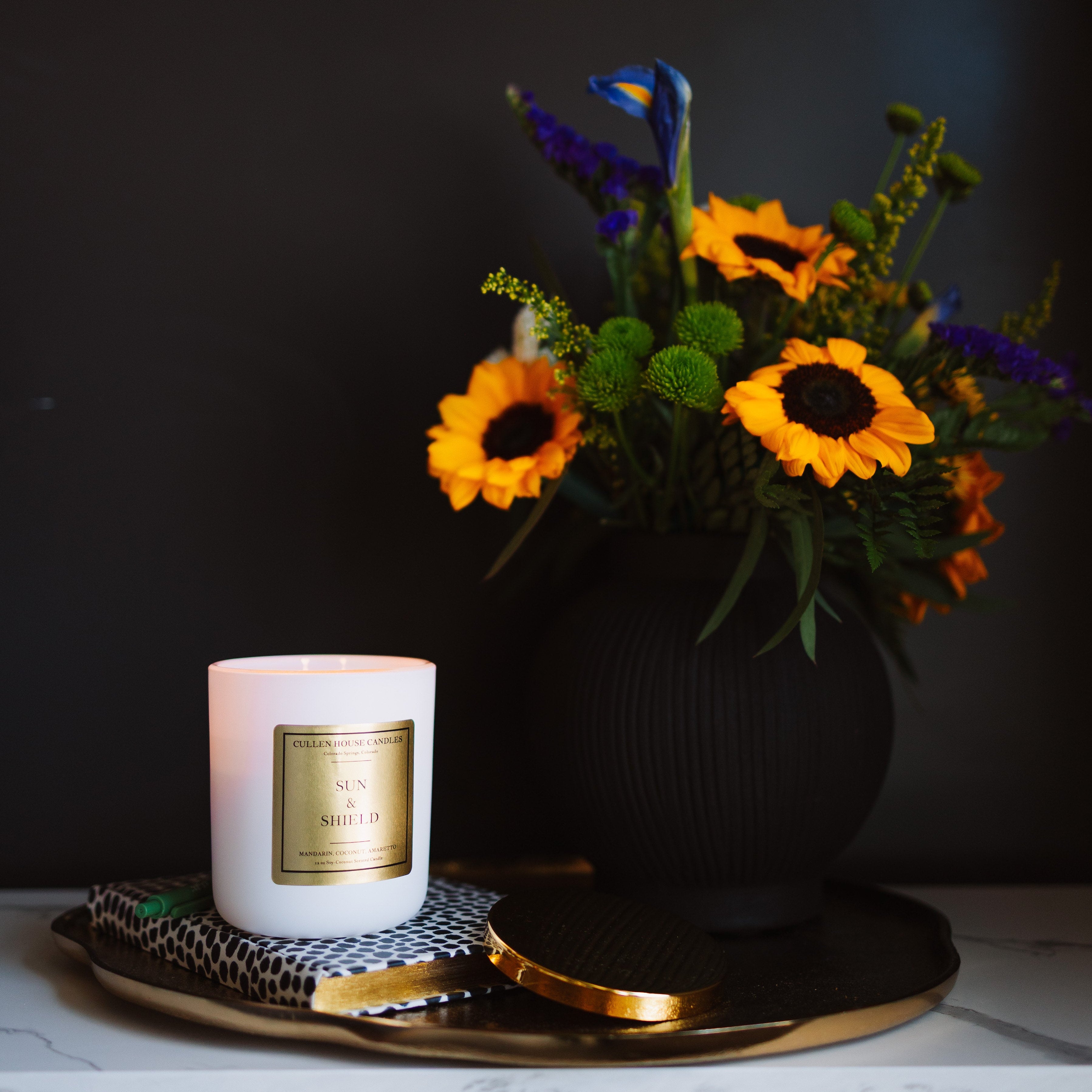 Candle with a decorative label and a vase of flowers on a dark background