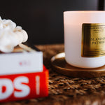 Candle with a gold label on a woven surface next to a book