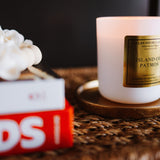 Candle with a gold label on a woven surface next to a book