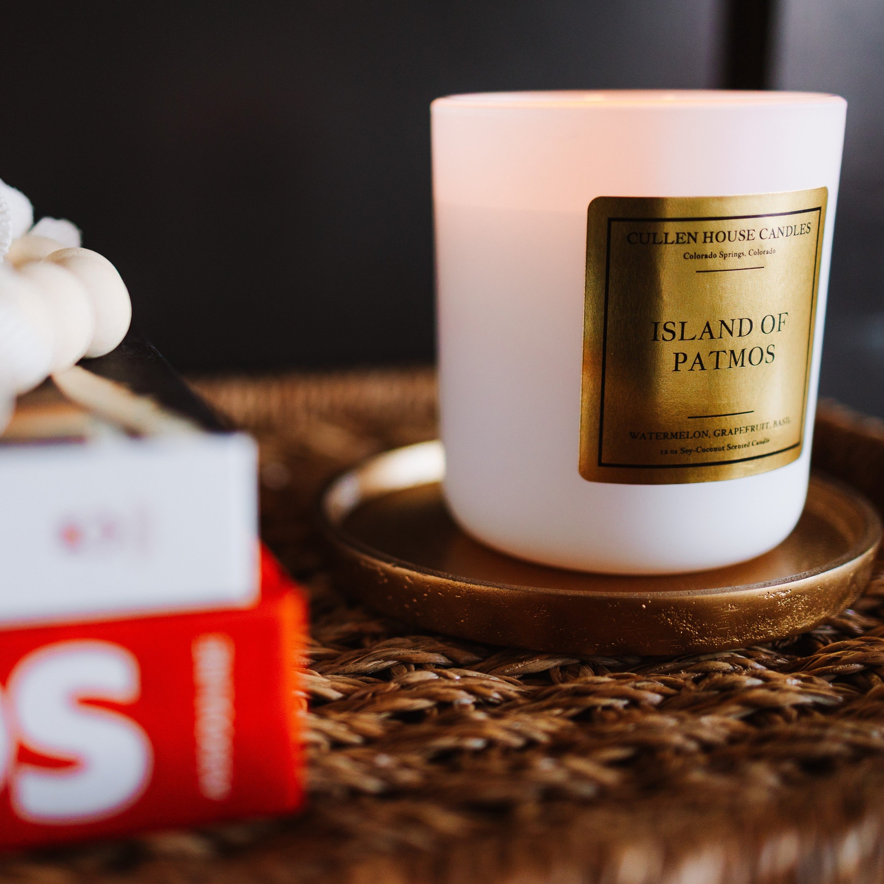 Candle with a gold label on a woven surface next to a book