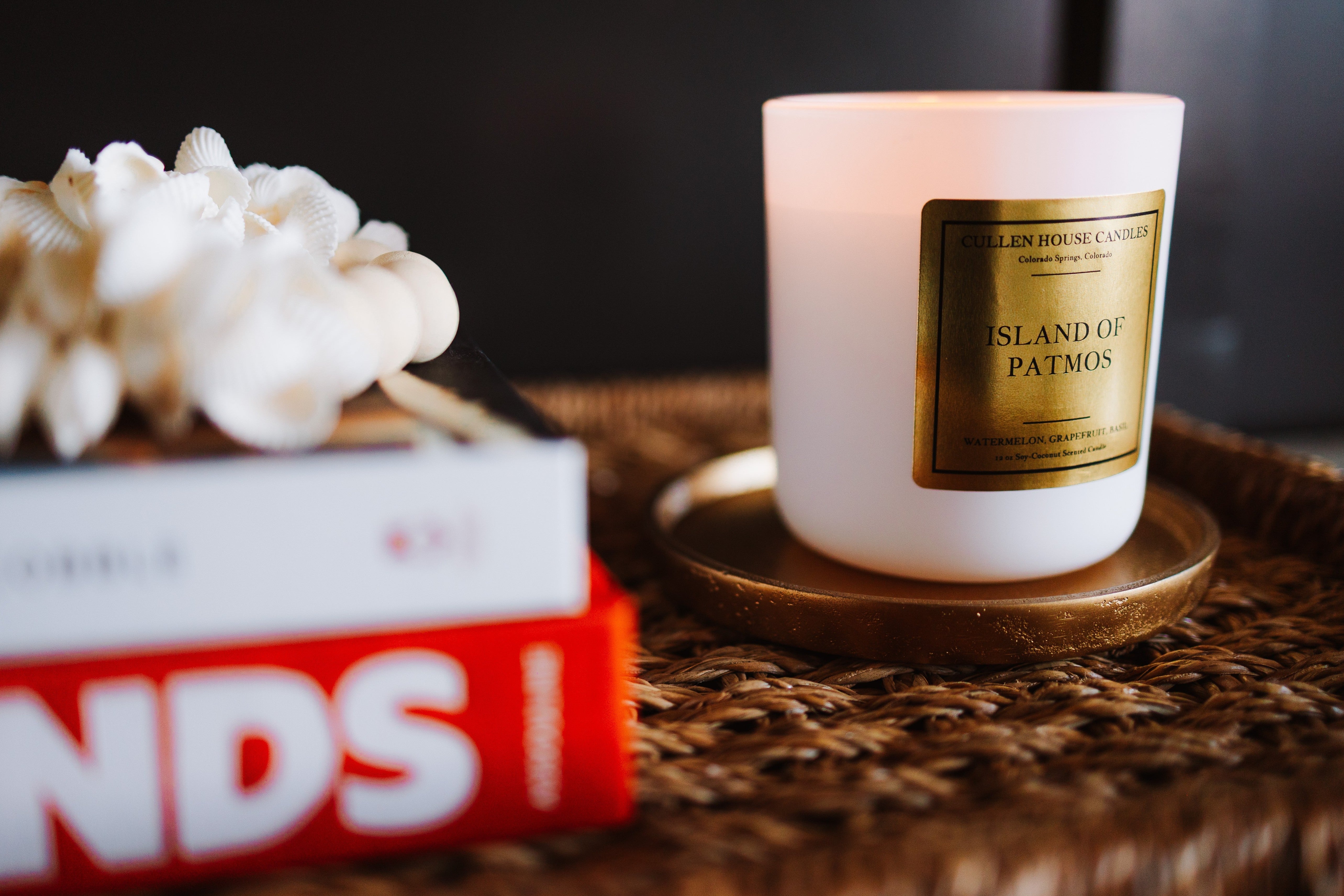 Candle with a gold label on a woven surface next to a book
