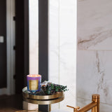 Bathroom sink with gold faucet and decorative candle on a marble shelf.