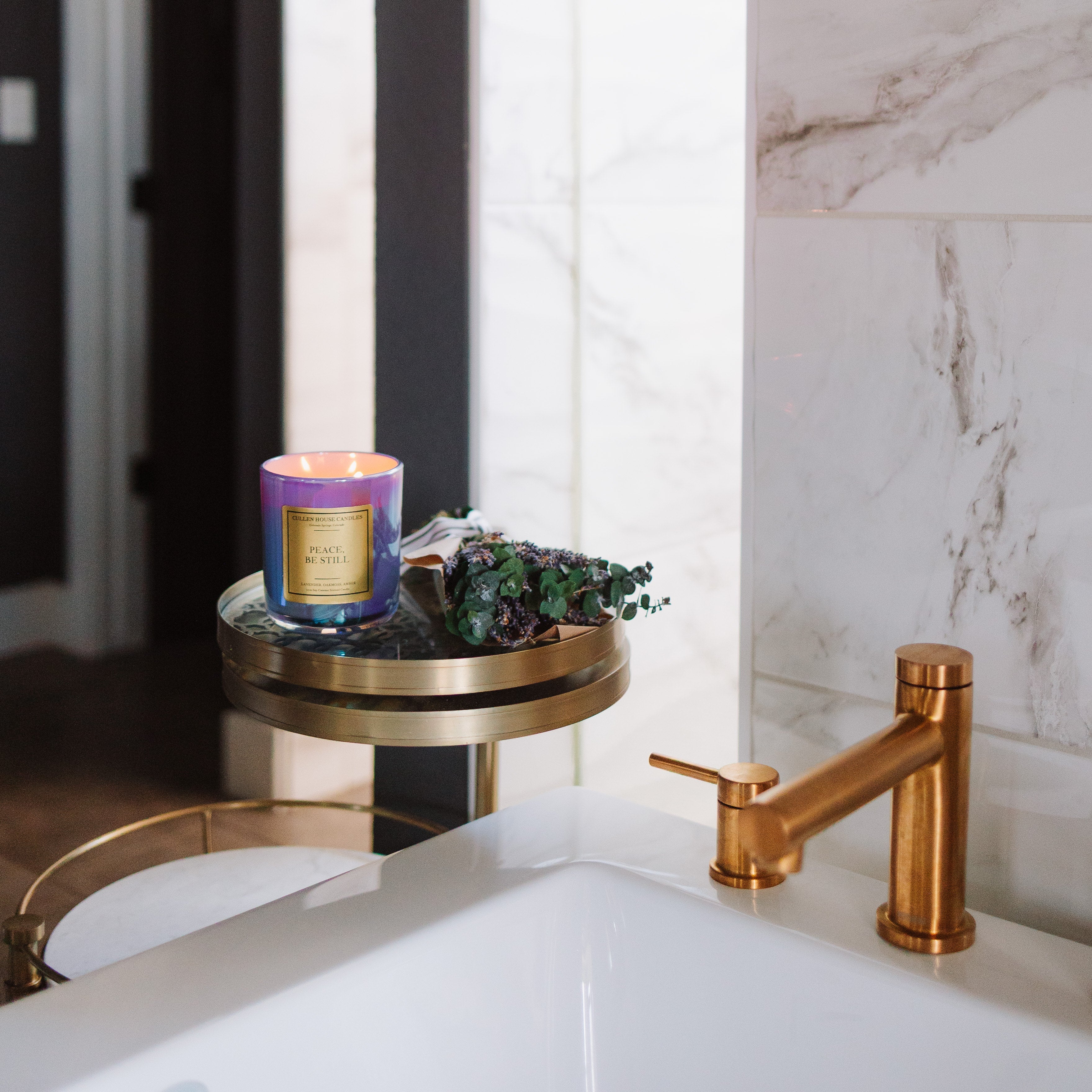 Bathroom sink with gold faucet and decorative candle on a marble shelf.