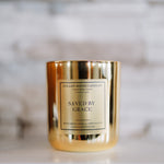 Candle with a gold holder and 'Saved by Grace' label on a blurred background