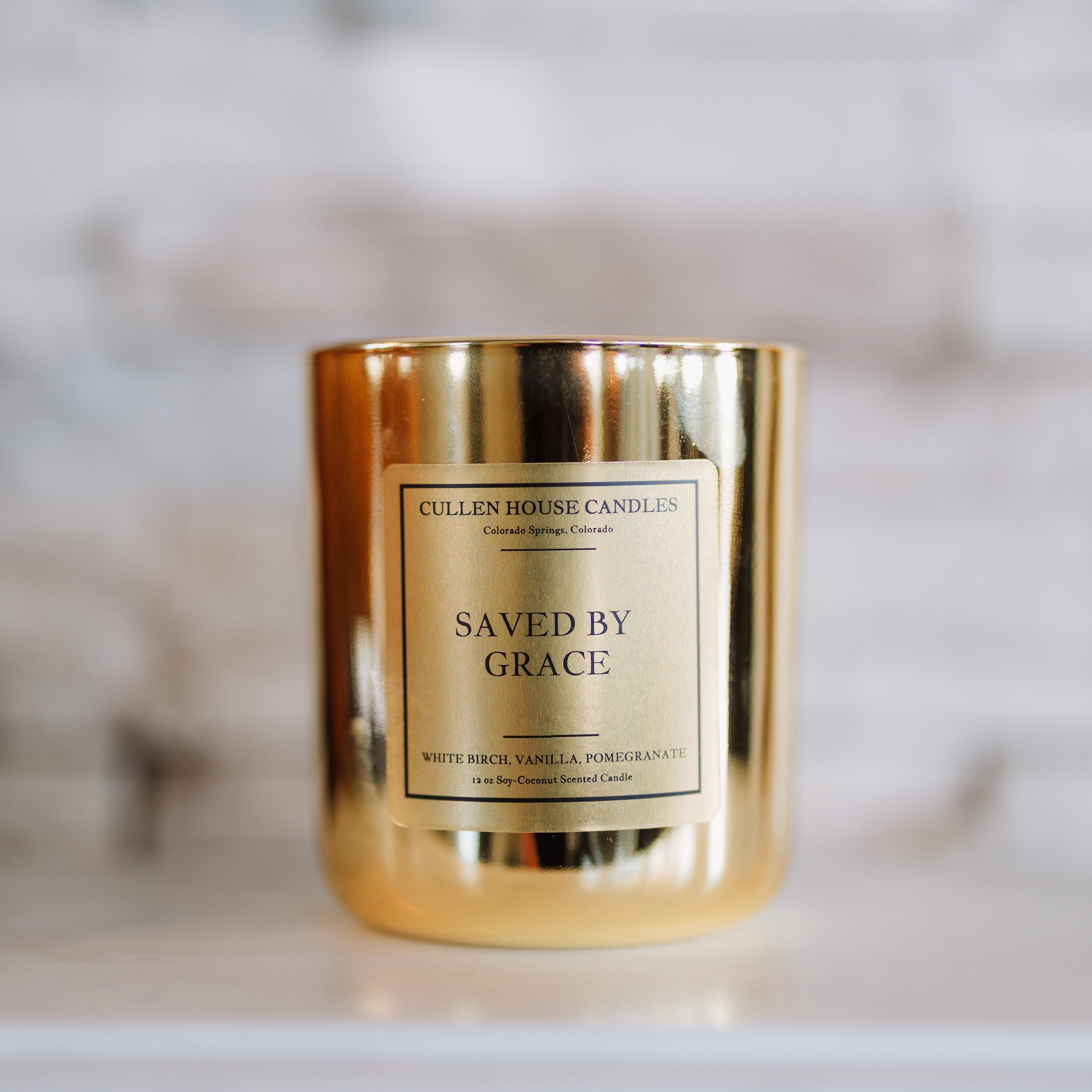 Candle with a gold holder and 'Saved by Grace' label on a blurred background