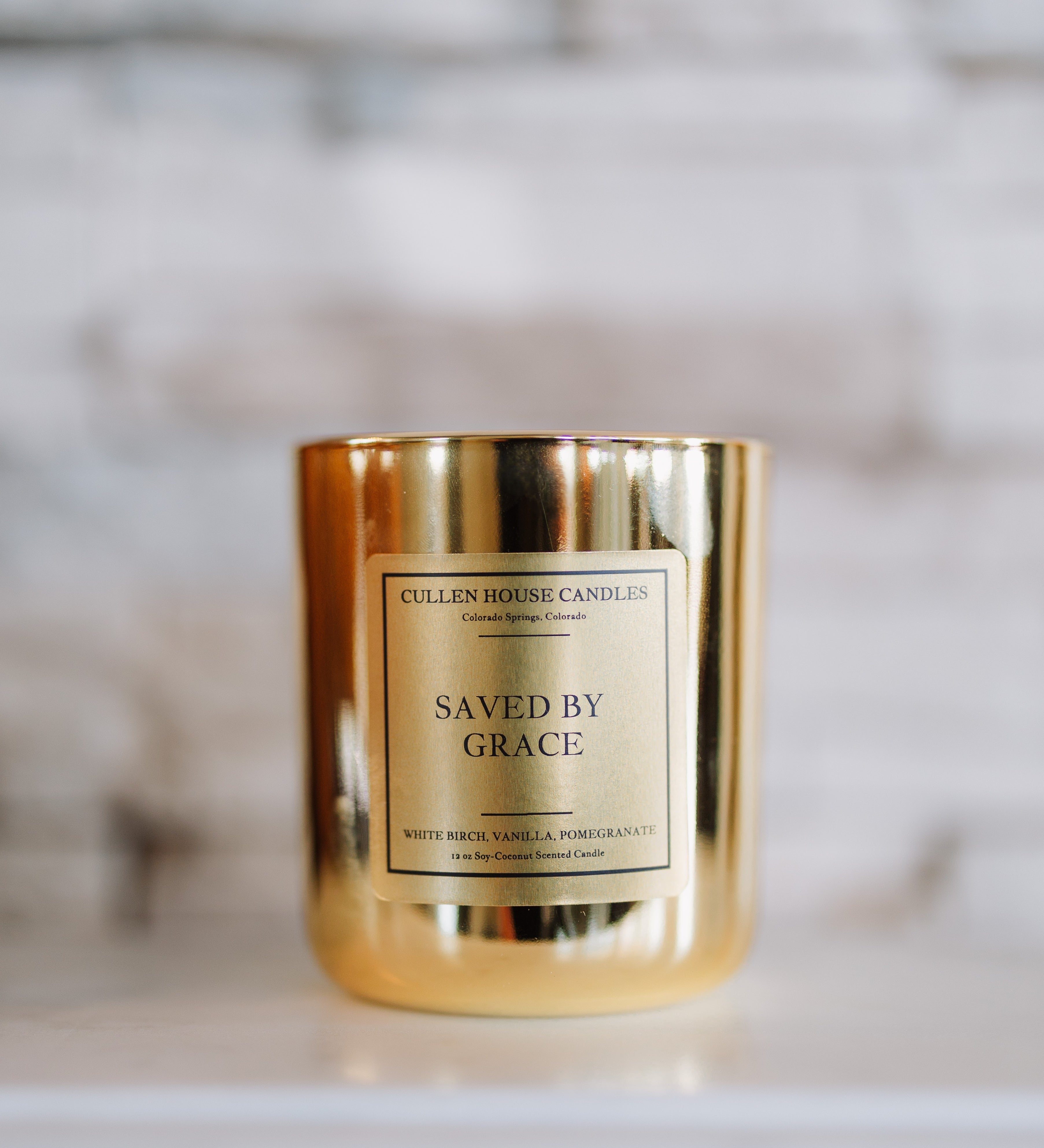 Candle with a gold holder and 'Saved by Grace' label on a blurred background